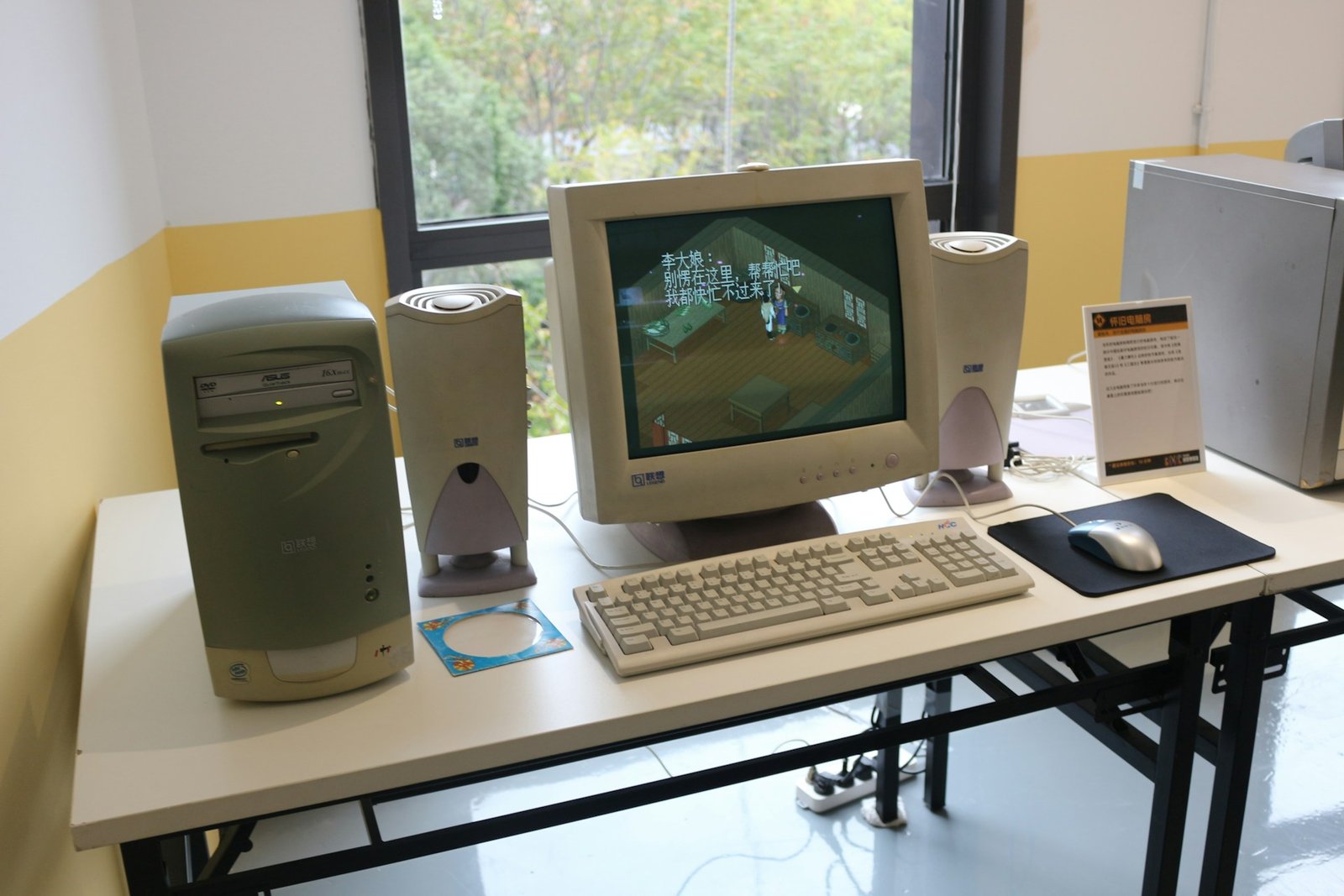 1990-luvun pöytäkone CRT-näytöllä, beige kotelo, näppäimistö, hiiri ja kaiuttimet valkoisella pöydällä ikkunan ääressä; hidas tietokone.