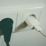 Puhelimen laturi ja tietokoneen virtajohto kytkettynä pistorasiaan, esimerkki kodin viihde-elektroniikan virrankulutuksesta.