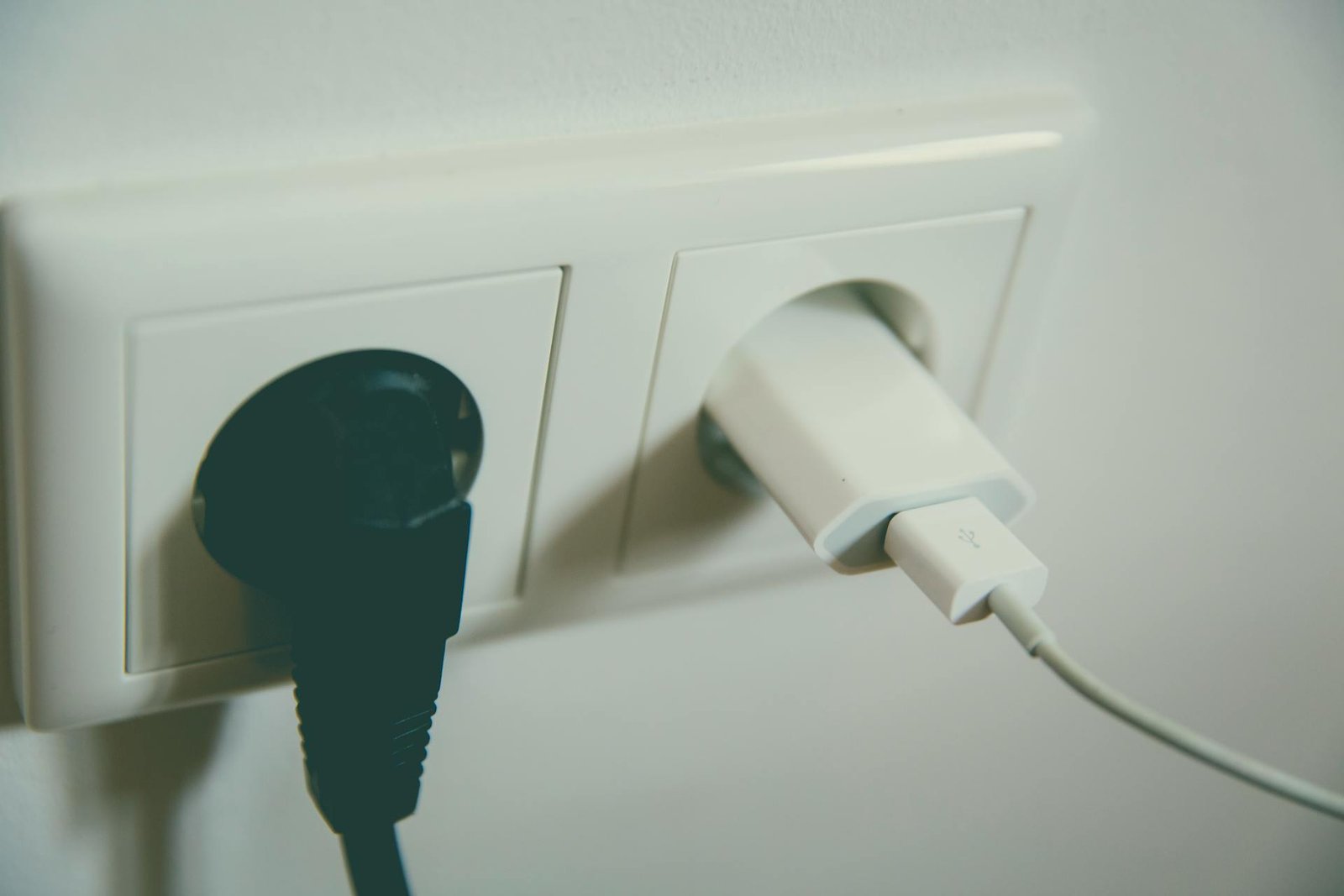 Puhelimen laturi ja tietokoneen virtajohto kytkettynä pistorasiaan, esimerkki kodin viihde-elektroniikan virrankulutuksesta.