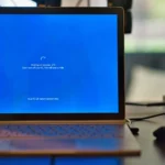 Kannettavan näyttö näyttää Windowsin päivityksen 27 %, sininen ruutu työpöydällä hiiren ja johtojen vieressä.